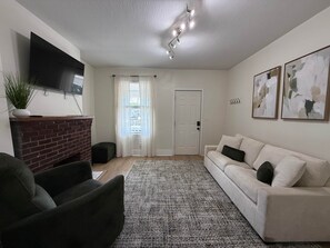 Ein Wohnzimmer mit Flachbildfernseher, Kamin aus Ziegeln, einer Couch, einem gemusterten Teppich und abstrakten Wandbildern.