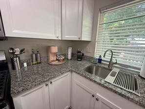 Eine Küche mit weißen Schränken, einer Arbeitsplatte aus Granit, einer Edelstahl-Spüle und einem Fenster mit Jalousien.