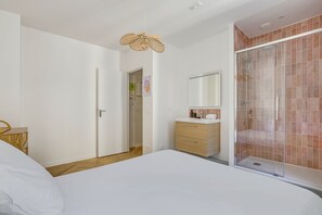 Ein Schlafzimmer mit einem Bett, einem Holzschrank, einem Spiegel, einer Duschkabine und einer Tür zu einem anderen Raum.