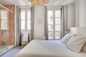 Camera d'albergo con letto, doccia, finestra con tende e vista sul balcone.