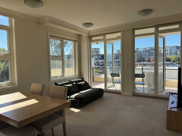 Een ruime woonkamer met een eettafel, bank en grote ramen met uitzicht op de stad.