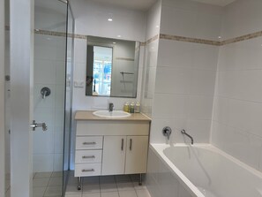 Een moderne badkamer met een douchecabine van glas, een witte wastafel met spiegel erboven en een vrijstaand bad.