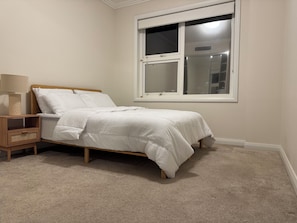 Een slaapkamer met een bed, nachtkastje, lamp en raam.