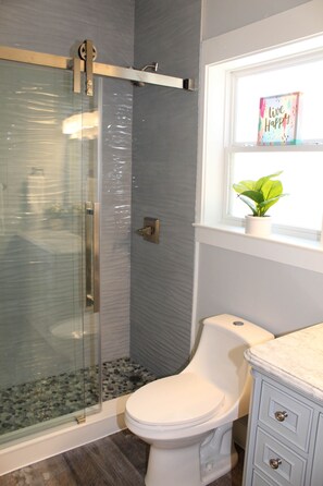 A bathroom with a glass-enclosed shower, a toilet, a vanity with drawers, and a window with a plant. - Beach Beyond Belief + Private pool+ free bikes (Rosemary Beach)