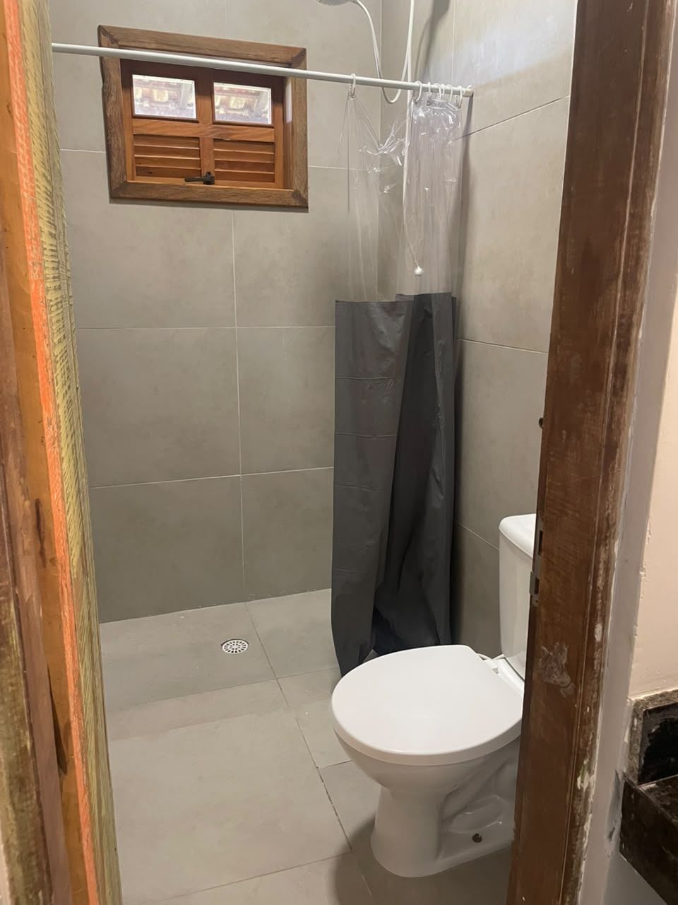 A bathroom with a toilet, a shower curtain, and a window with shutters.