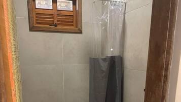 A bathroom with a toilet, a shower curtain, and a window with shutters.