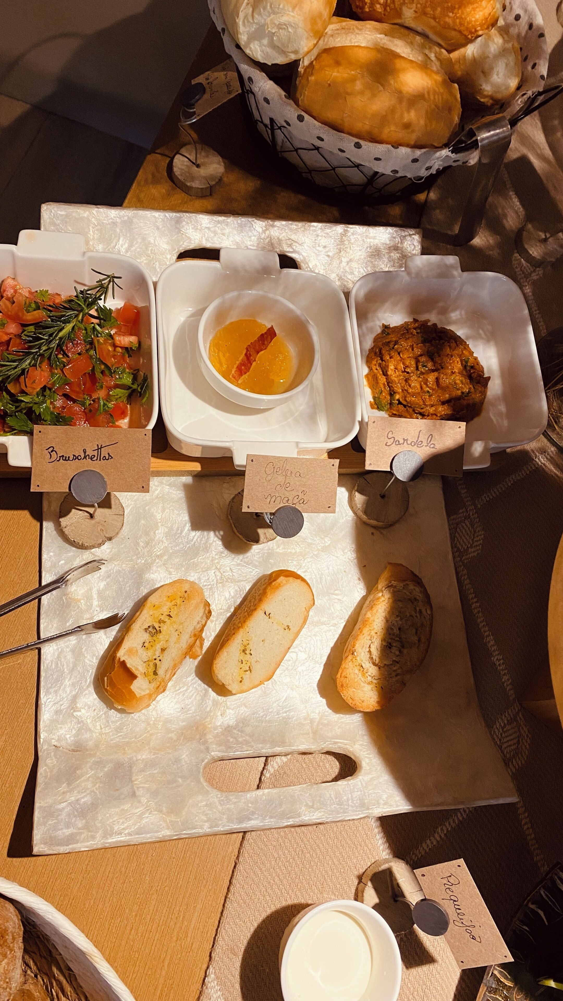 A table with various food items and bread, including Bruschettas, Gelatina de Maza, and Sándela.