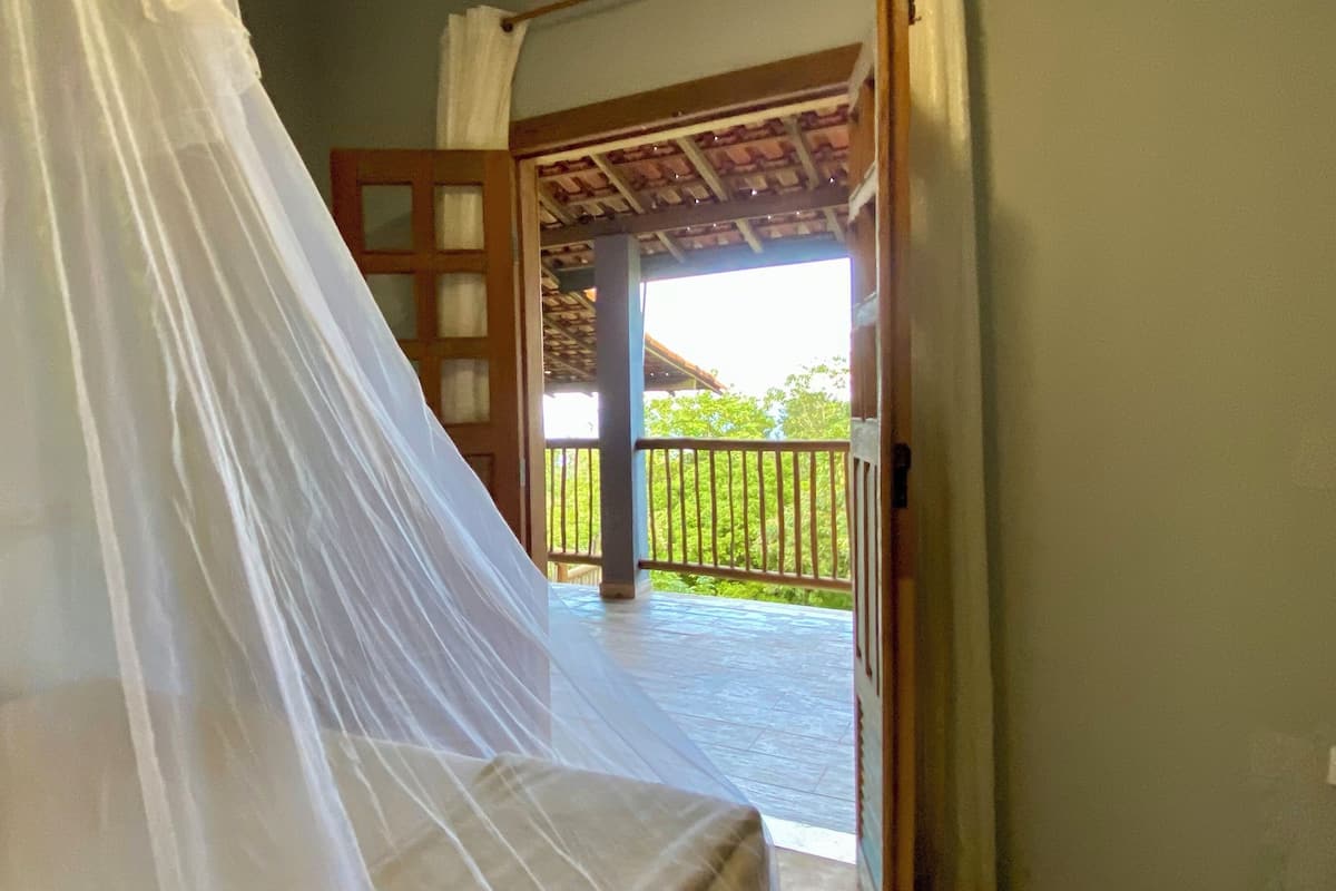 A room with a bed covered in a white canopy, a wooden door, and a view of a balcony with a railing.