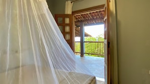 A room with a bed covered in a white canopy, a wooden door, and a view of a balcony with a railing. - Pousada Refúgio da Ilha (Ilhabela)