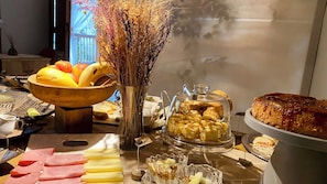 A buffet table with various food items including fruits, bread, and pastries. - Pousada Refúgio da Ilha (Ilhabela)