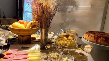 Una mesa de buffet con diversas opciones de comida, incluyendo frutas, pan y pasteles.