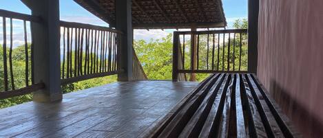 A wooden deck with railings, a bench, and a view of greenery.