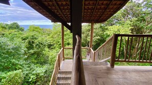Eine Holztreppe führt zu einem überdachten Bereich mit Blick auf dichtes Grün und das Meer.