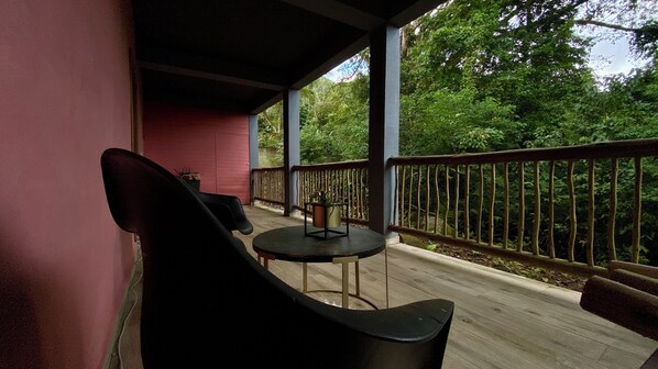 Ein überdachter Außenbereich mit Tisch und Stühlen, einem Geländer und Blick auf dichtes Grün.