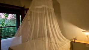A room with a bed under a canopy, a balcony with a railing, and a nightstand with a lamp.
