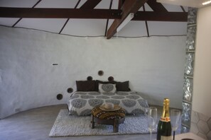 A bedroom with a bed, a small table with a bottle and glasses, and a decorative wall.