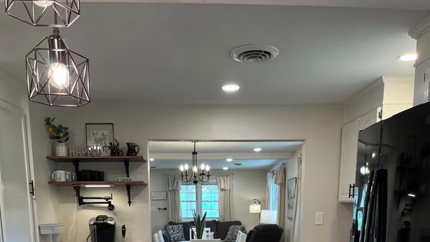 Una cocina moderna con una isla de madera, un comedor con candelabro y un refrigerador negro.