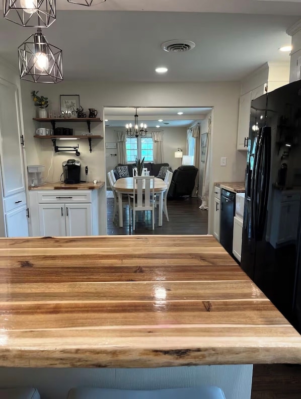 A modern kitchen with a wooden island, a dining area with a chandelier, and a black refrigerator.