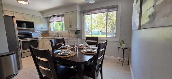 A modern kitchen with white cabinets, a dining table set for four, and a large window with a view of the outdoors.