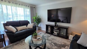 Un salon avec un canapé noir, une table basse en verre, un téléviseur fixé au mur et une plante posée sur la table.