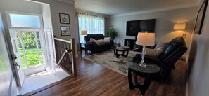 Sala de estar con sofá, mesa de centro y televisión. Una escalera conduce a un área exterior con vistas.