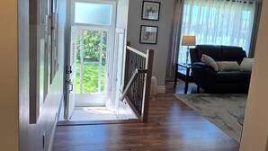 Un couloir au plancher de bois, un escalier menant à un balcon et un espace de vie comprenant un canapé et une lampe.