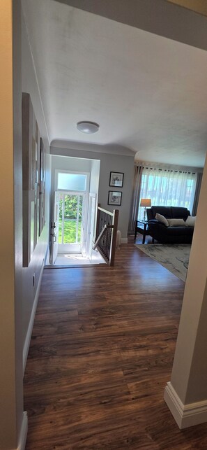Un pasillo con suelo de madera, una escalera que lleva a un balcón y una sala de estar con sofá y lámpara.