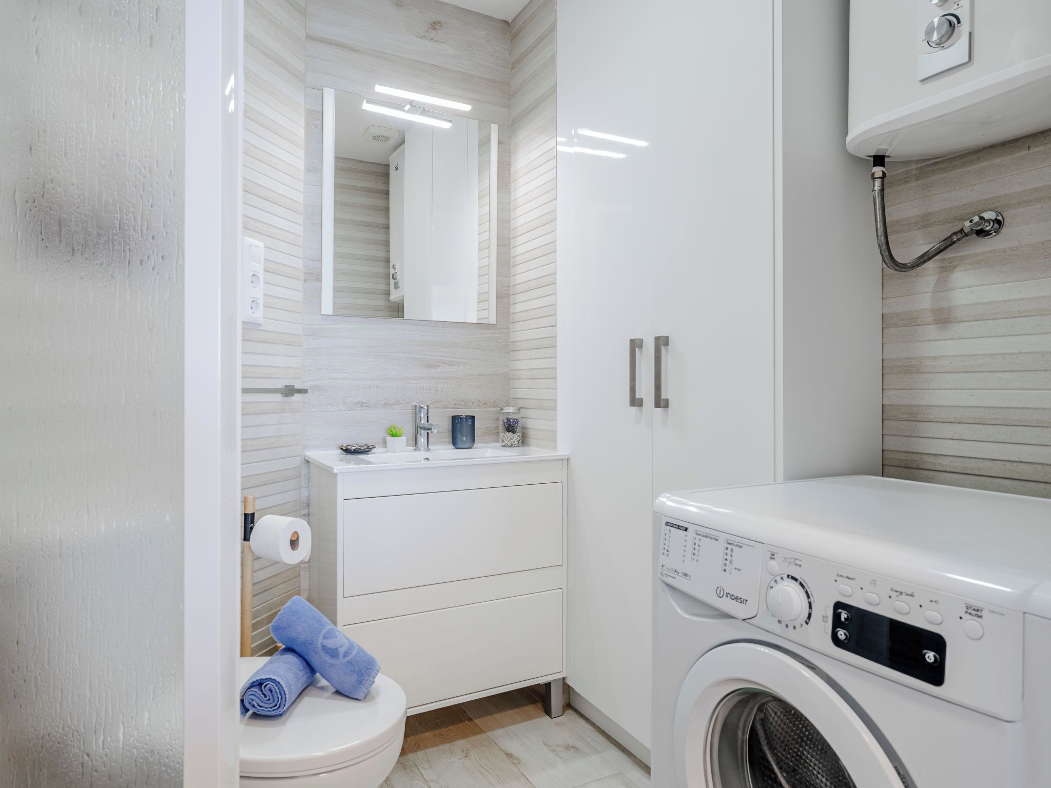 A modern bathroom with a white sink, mirror, and a washing machine.
