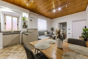 Een moderne keuken met een houten plafond, een eethoek met een houten tafel en stoelen, en een zithoek met een bank en een plant.