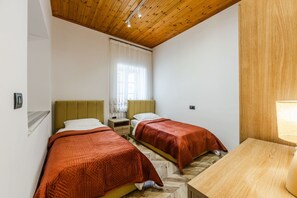 Ein Zimmer mit zwei Betten, Holzboden, weißen Wänden und einem kleinen Tisch mit einer Lampe.