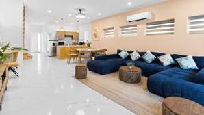 A modern living room with a blue sofa, a dining area, and a kitchen in the background. - The Luxe A5 | Beachside @ The Drake Residences (Simpson Bay)
