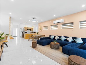 Una sala de estar moderna con un sofá azul, una zona de comedor y una cocina al fondo.