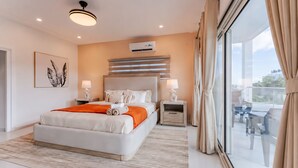 A modern hotel room with a large bed, bedside tables, an air conditioning unit, and a balcony with outdoor seating. - The Luxe A5 | Beachside @ The Drake Residences (Simpson Bay)