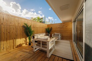 Um deck de madeira com um sofá branco e uma mesinha, um vaso de planta e vista do céu.