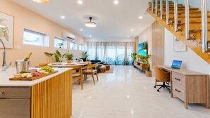 A modern kitchen with a wooden island, dining area, and a staircase leading to an upper level. - The Luxe A5 | Beachside @ The Drake Residences (Simpson Bay)