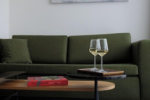 Un sofá verde, una mesita redonda con un libro y dos copas de vino blanco.