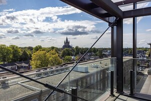 Un edificio alto con vistas a una estructura distante que parece un castillo, un balcón de vidrio y un cielo despejado.