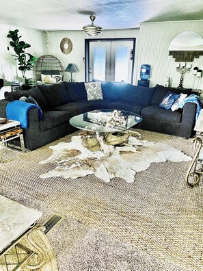 A living room with a dark-colored sofa, a glass coffee table, and a patterned rug.