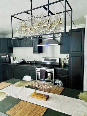 A modern kitchen with dark cabinetry, a central island, and a decorative chandelier.