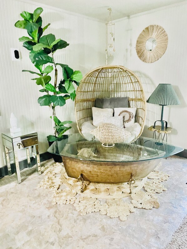 A room with a glass-bottomed chair, a hanging plant, a lamp, and a decorative mirror.