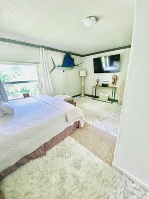 A bedroom with a bed, a flat-screen TV, a decorative fish on the wall, and a window with curtains.