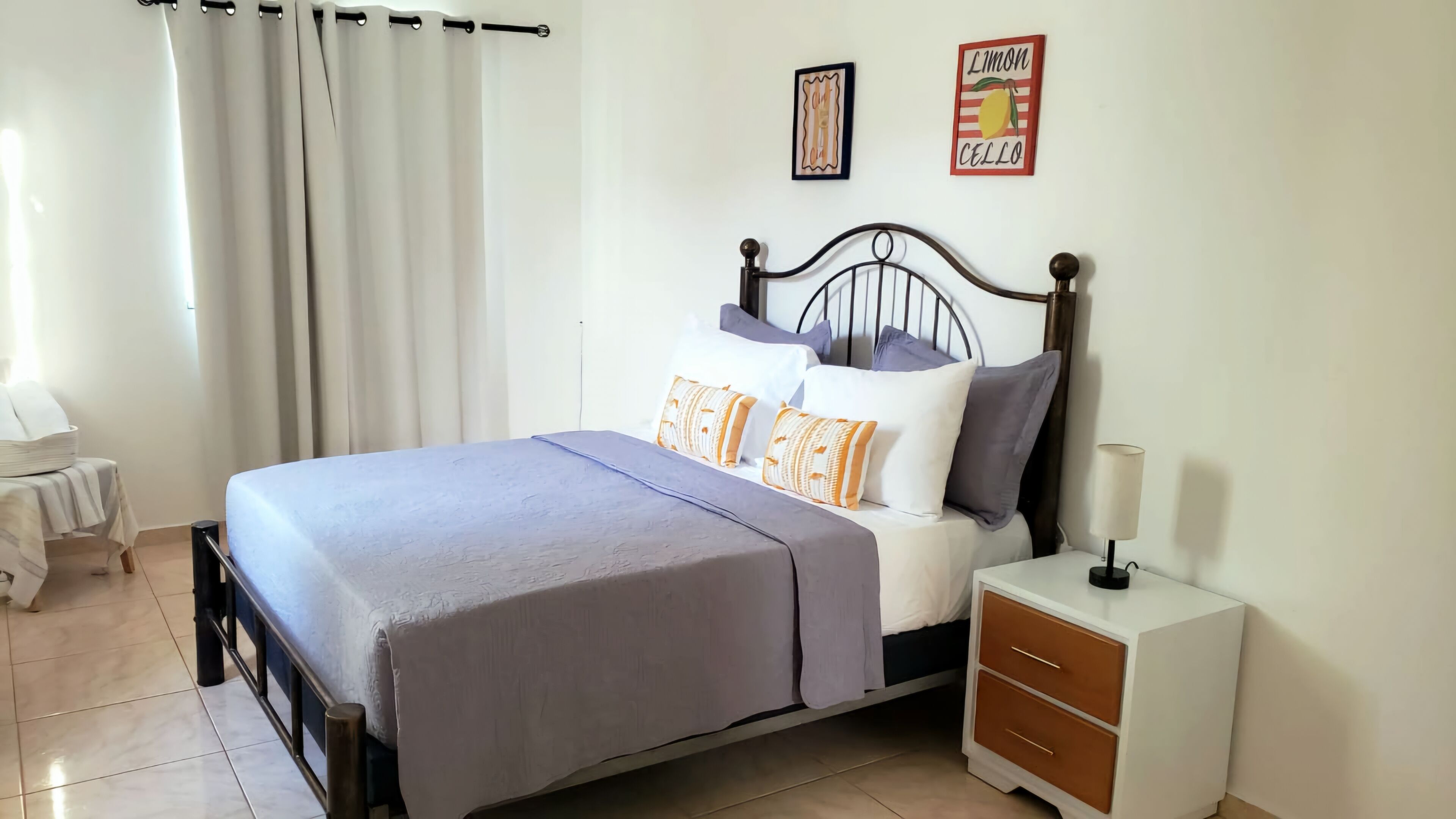 A neatly made bed with a grey bedspread, a bedside table with drawers, and a wall-mounted lamp.