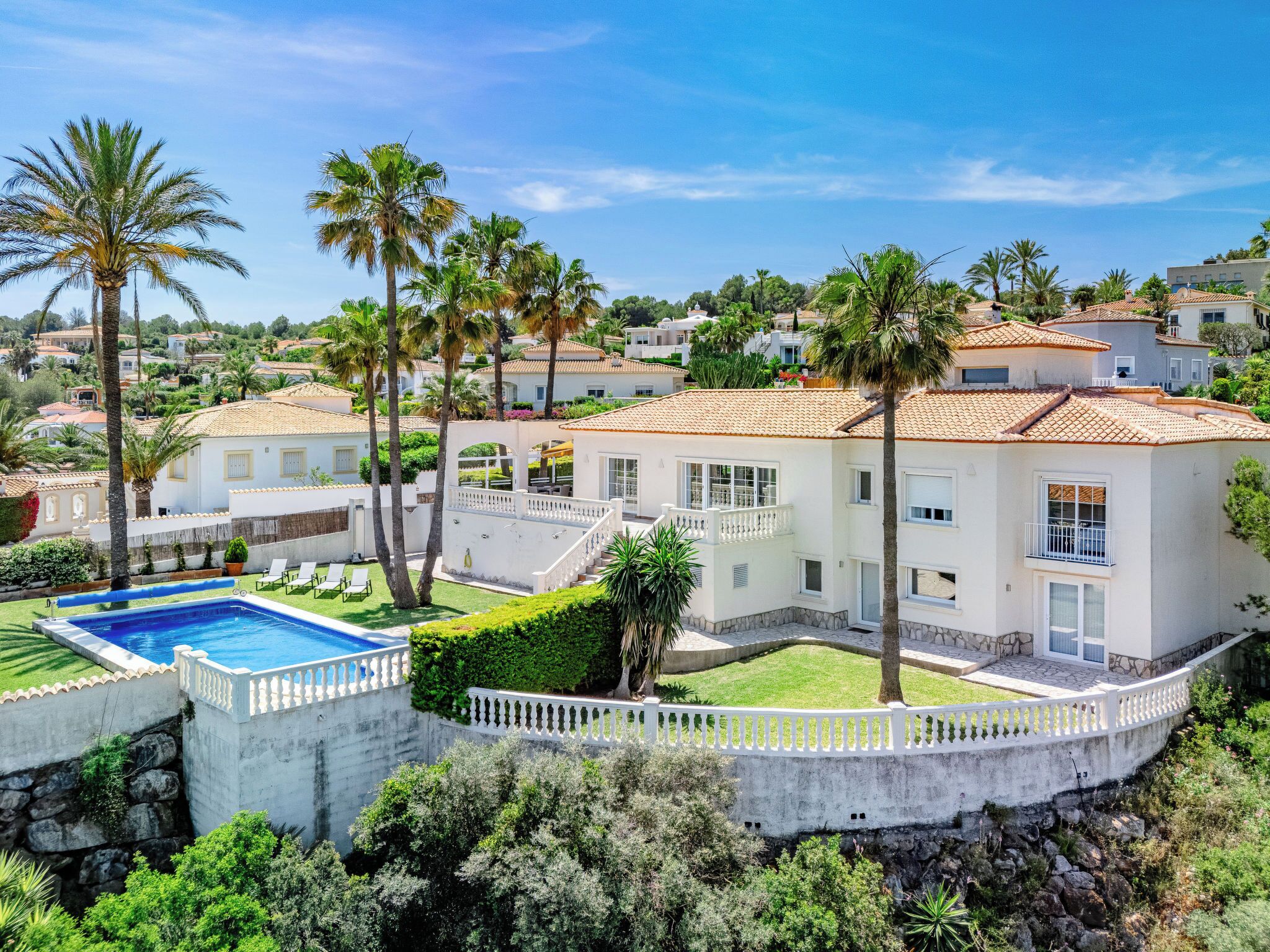 A white villa with a pool, surrounded by palm trees and a stone wall.