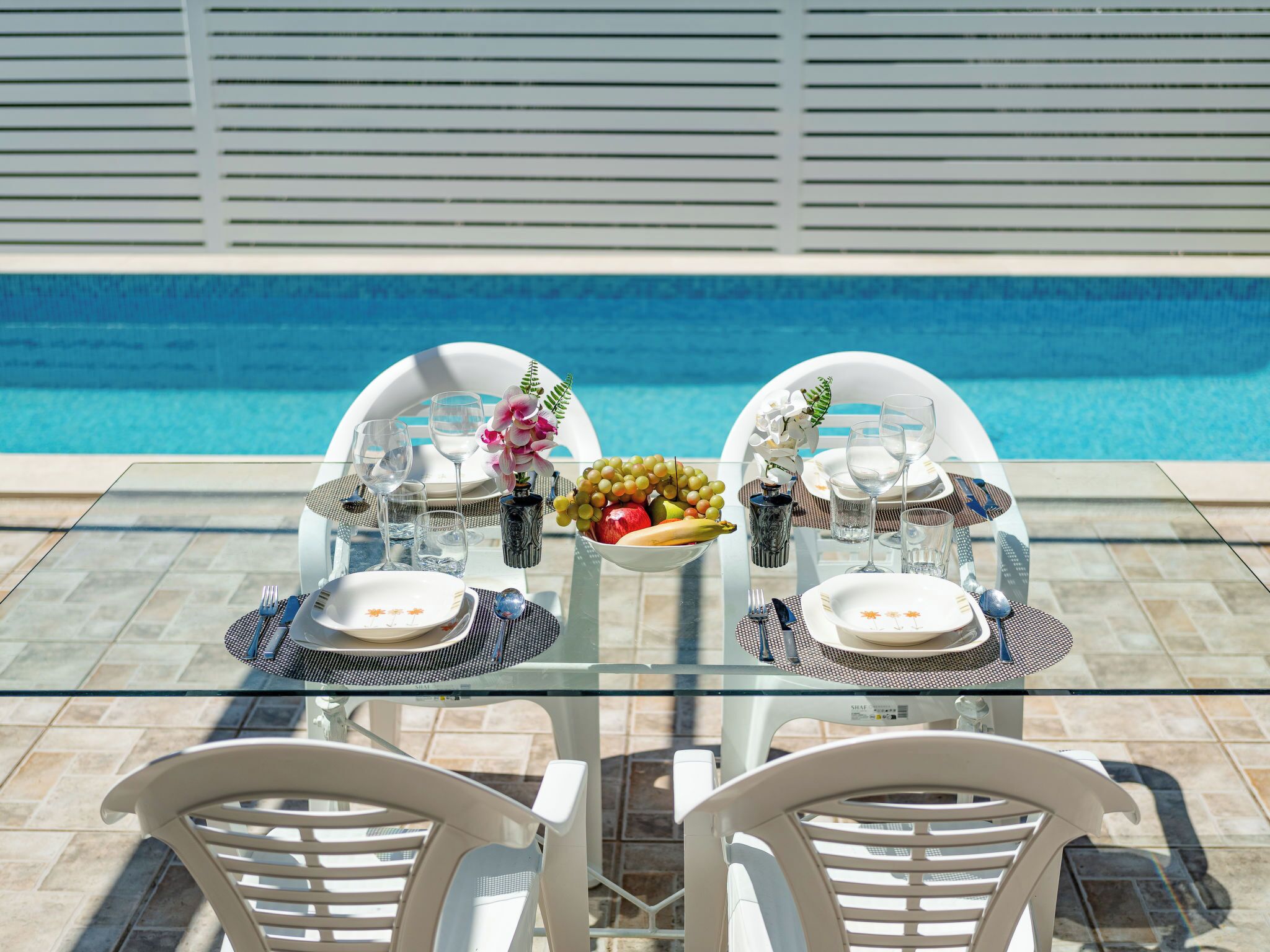 A dining table with chairs, a fruit bowl, and a pool in the background.