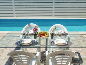 Ein Esstisch mit Stühlen, einer Obstschale und einem Pool im Hintergrund.