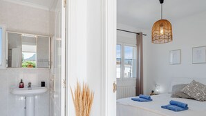 Une chambre à coucher comprenant un lit, une table de chevet, une fenêtre et une salle de bain avec un lavabo et un miroir.