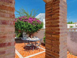 Eine Terrasse mit Tisch und Stühlen, eine Ziegelwand und ein Busch mit rosa Blüten.