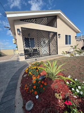 Ein modernes, zweistöckiges Gebäude mit einer geometrischen Fassade, einem verschlossenen Eingang und einem angelegten Garten mit Blumen und Pflanzen.