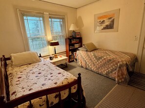 A bedroom with two beds, a nightstand, a lamp, a bookshelf, and a framed picture on the wall. - Cozy 1-bedroom bungalow in East Atlanta (Atlanta)