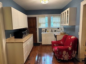 A compact kitchen with white cabinets, a microwave, and a red chair with floral upholstery. - Cozy 1-bedroom bungalow in East Atlanta (Atlanta)